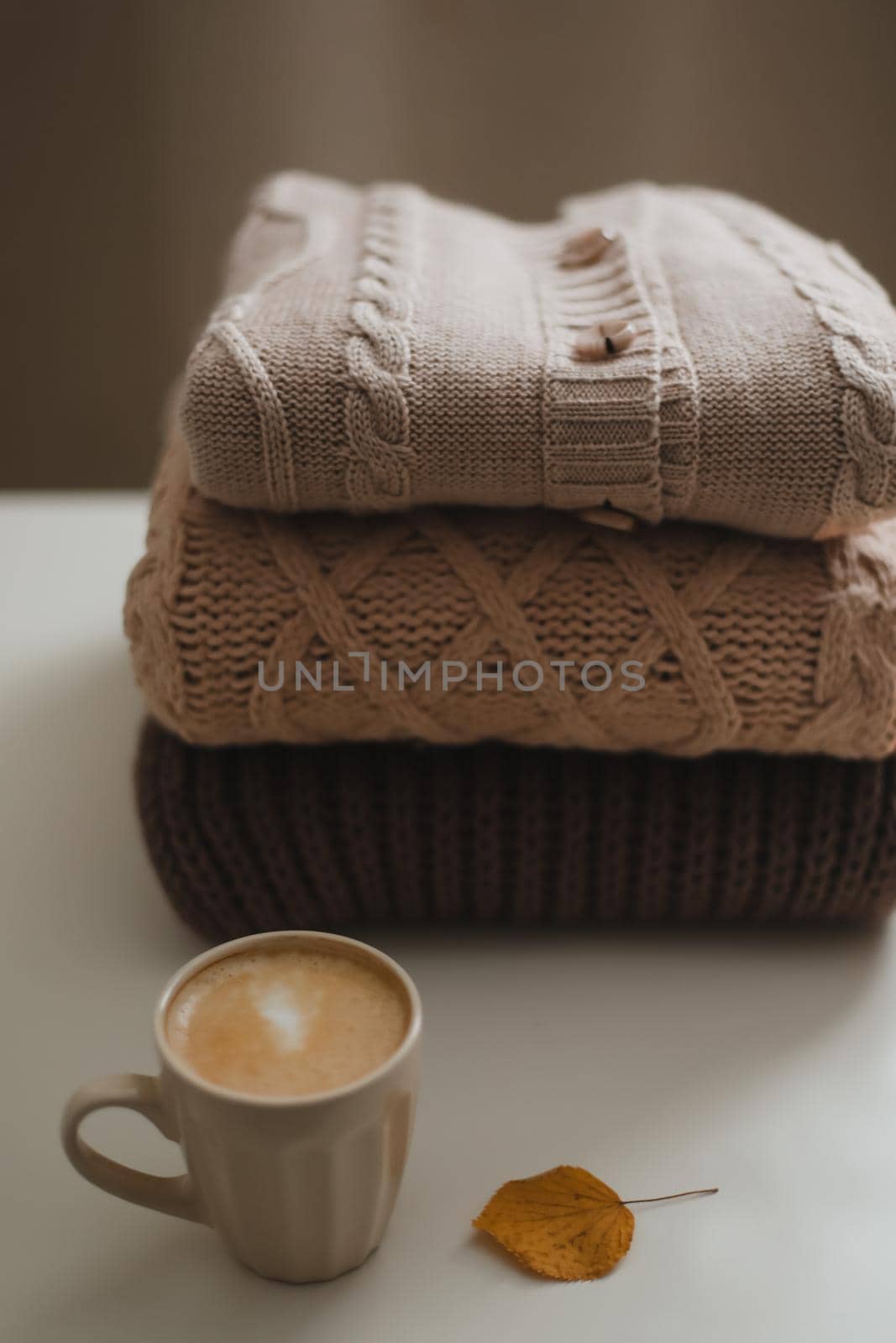 cozy home atmosphere and still life with a cup, candle and sweaters on a table.