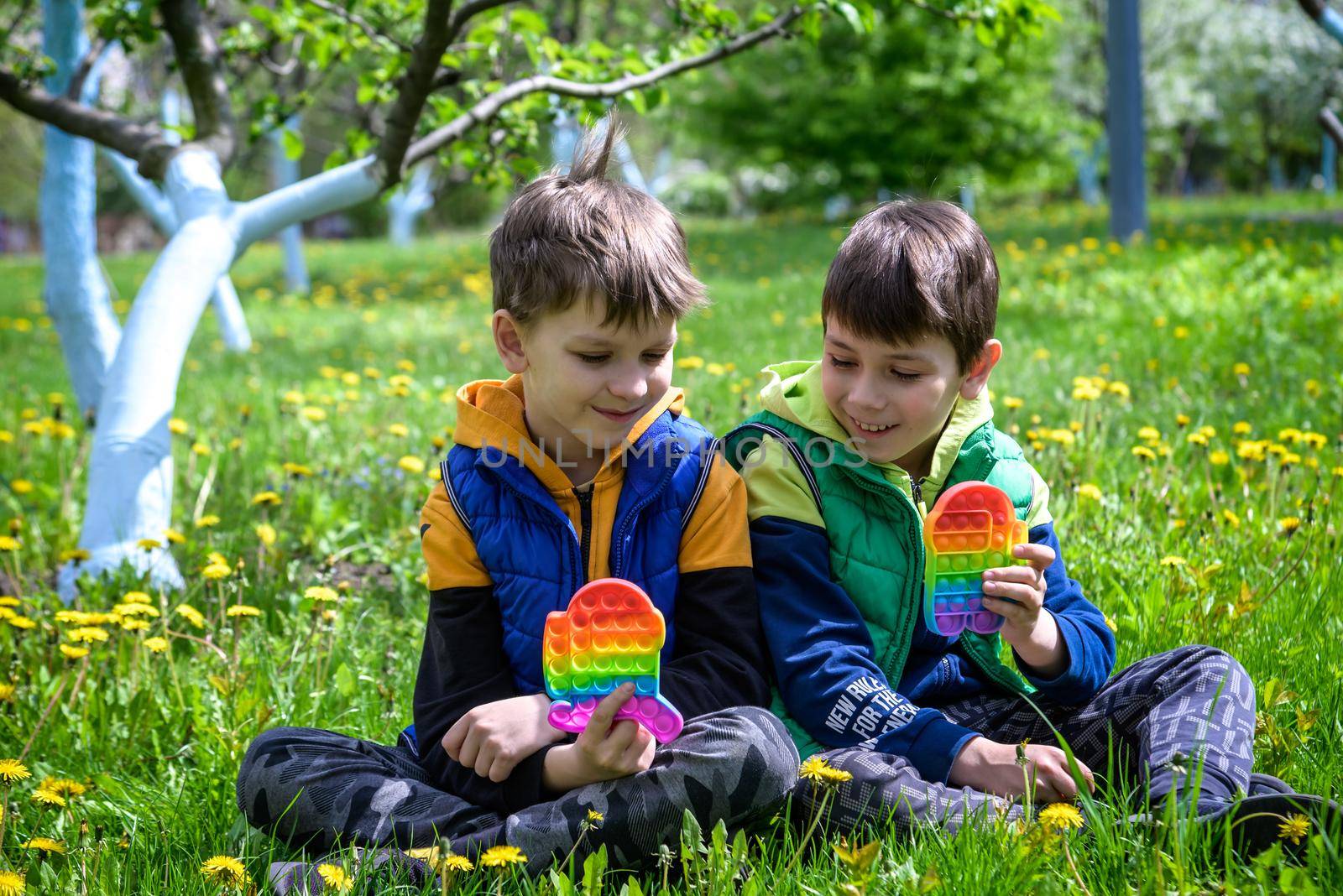 children playing with colorful toys Pop It. Boys on vacation. Tired of games, relaxing on the grass. Summer time for children, two boys friends at reboot together by Kobysh