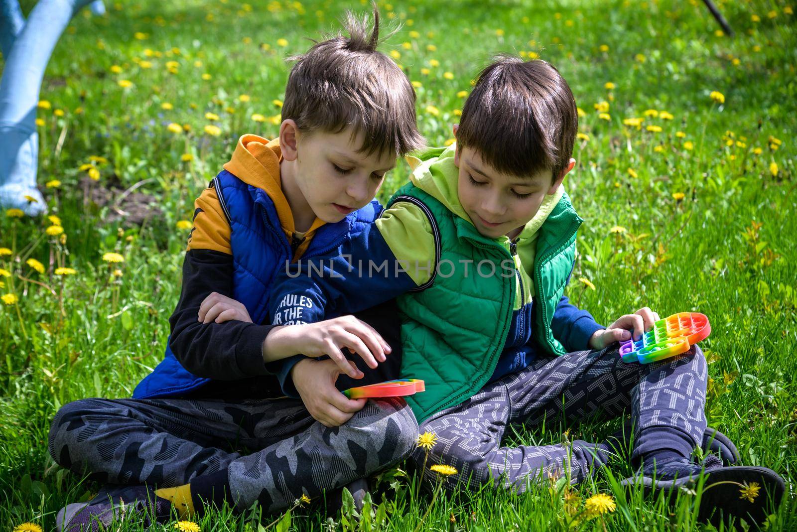 children playing with colorful toys Pop It. Boys on vacation. Tired of games, relaxing on the grass. Summer time for children, two boys friends at reboot together.