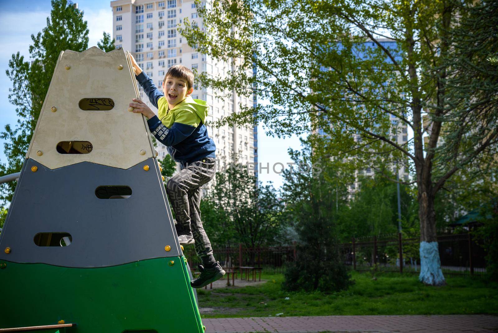 Teenager boy climbing at kid playground outdoor. The climber trains simulator on the street. Healthy leisure for children concept.