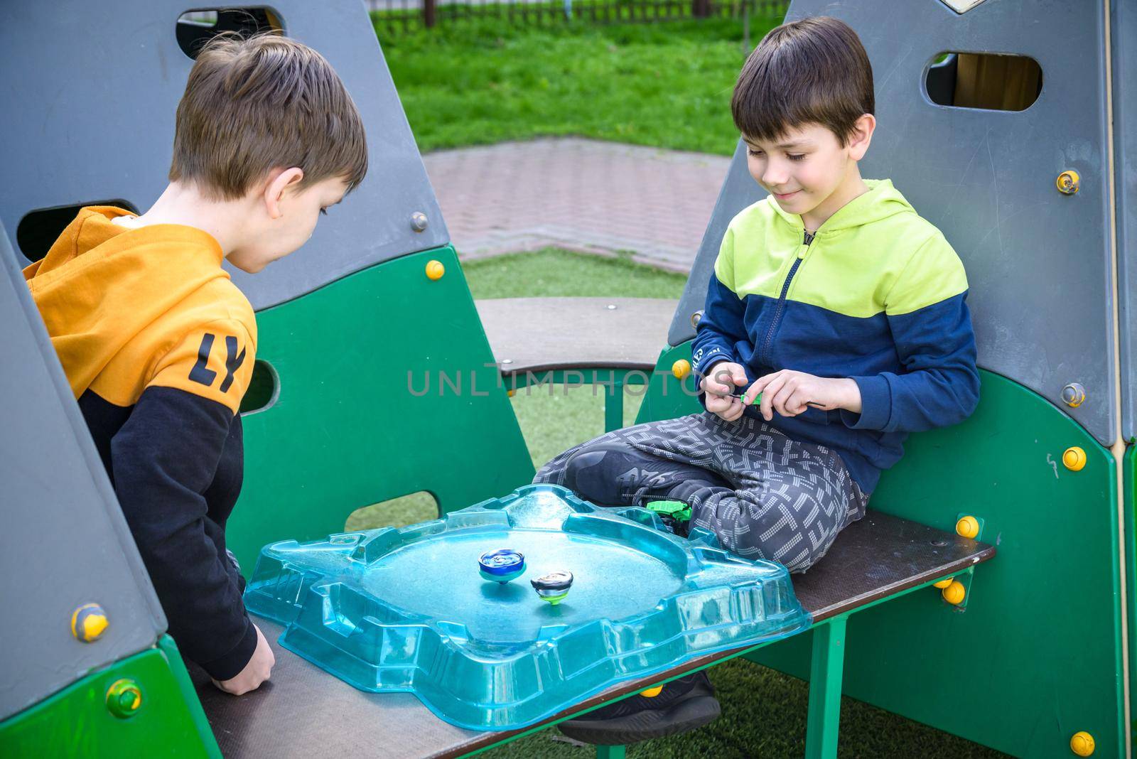 Two Boys playing with modern spin top outdoors. Entertainment game for children. Top, triggered by a trigger. Kids having a tournament on arena or battle field by Kobysh
