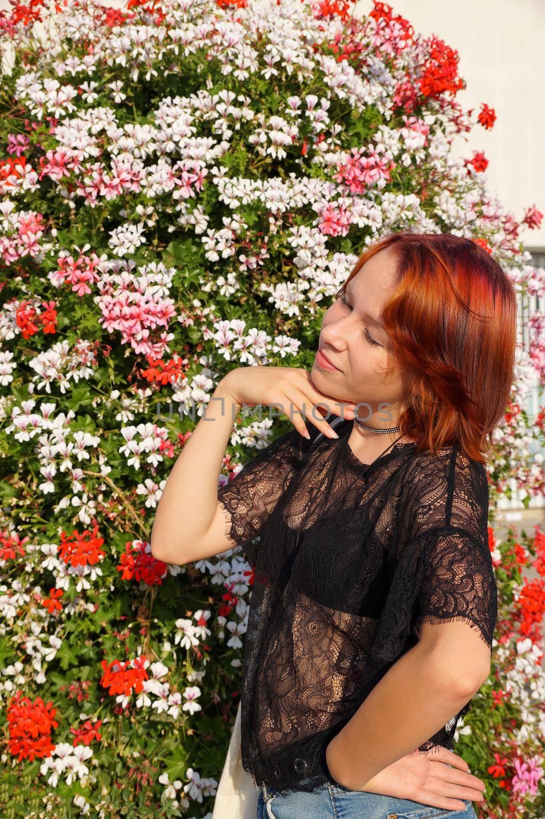 portrait of a smiling red-haired teenage girl with closed eyes on a floral background in the sunlight.