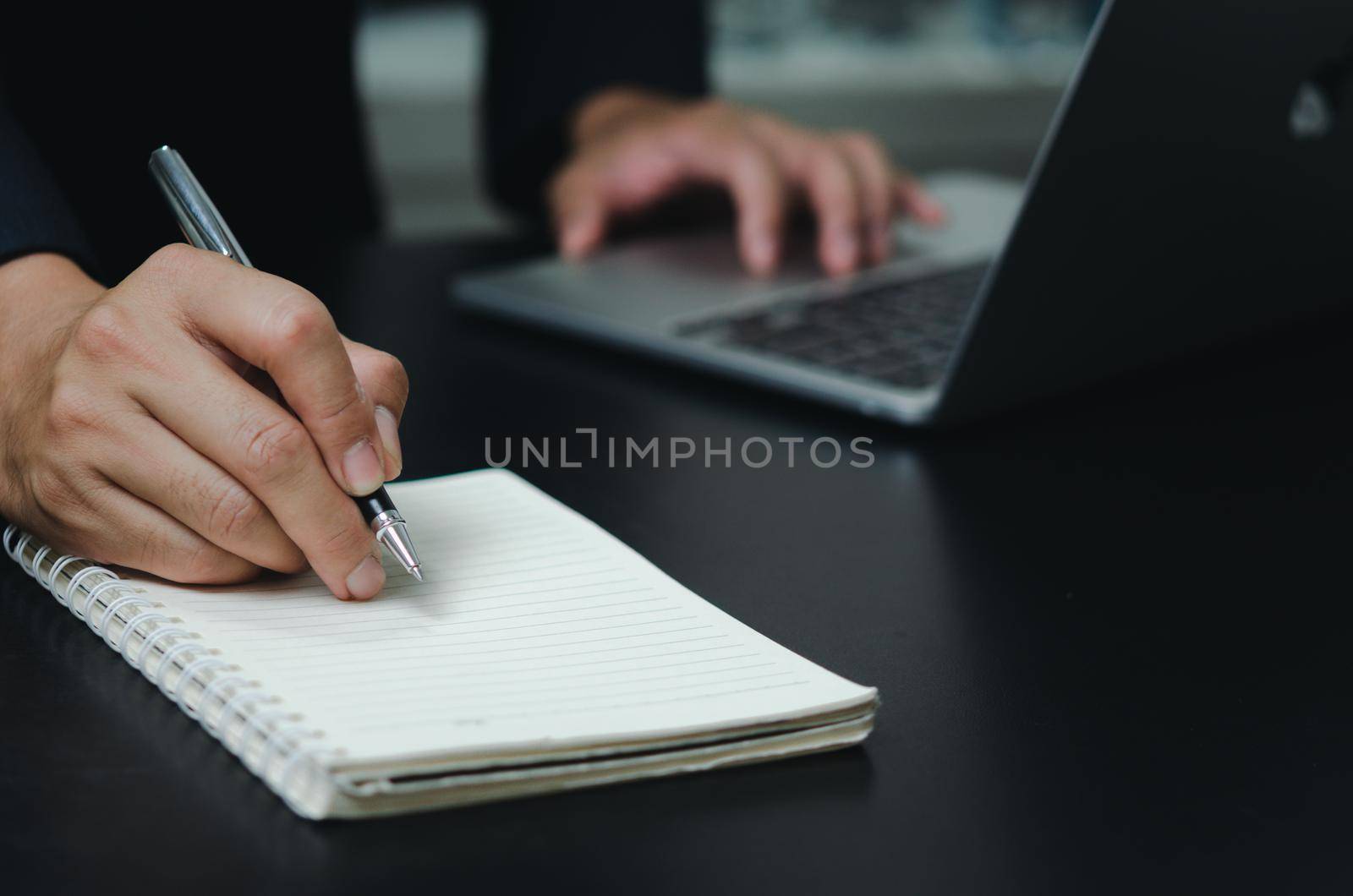 Businessman holding pen writing book note on desk with computer laptop.