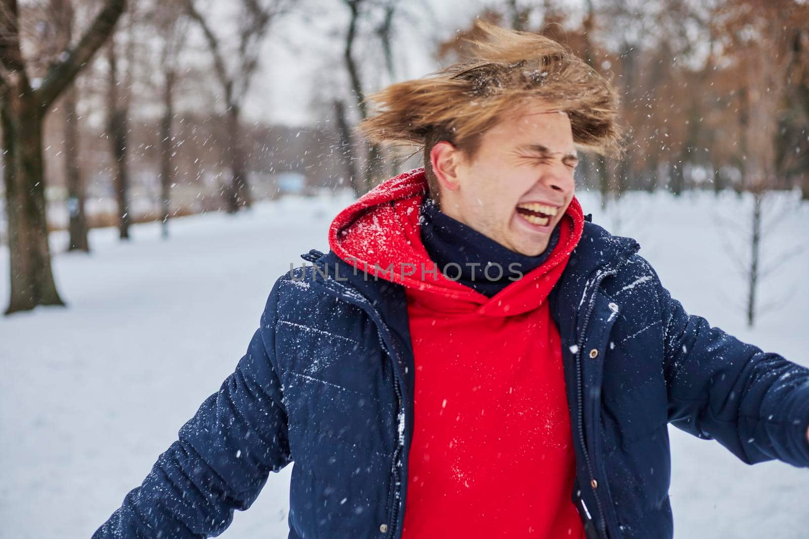 a young happy man is having fun in a winter park, throwing snow, it is cold in his hands, the emissions are off scale