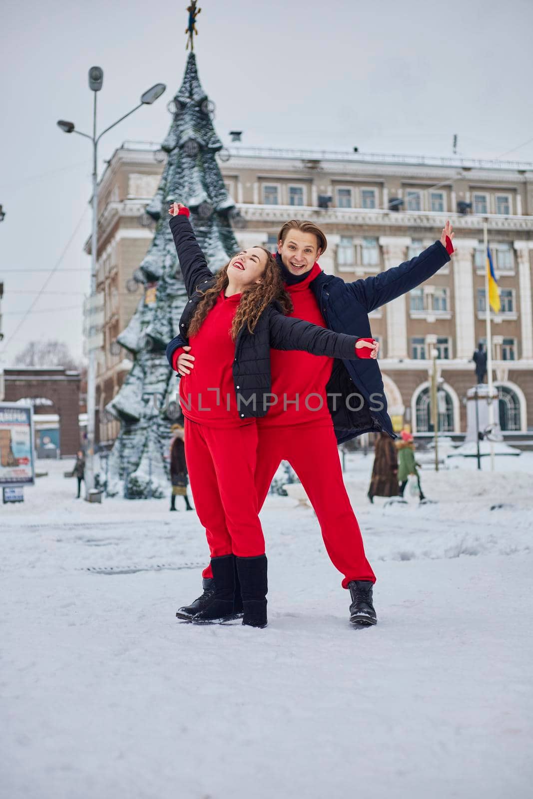 young family guy and girl spend the day in the park on a snowy day. Emotional young couple having fun while walking in the winter city, a lively man hugs his laughing beautiful woman. by mosfet_ua