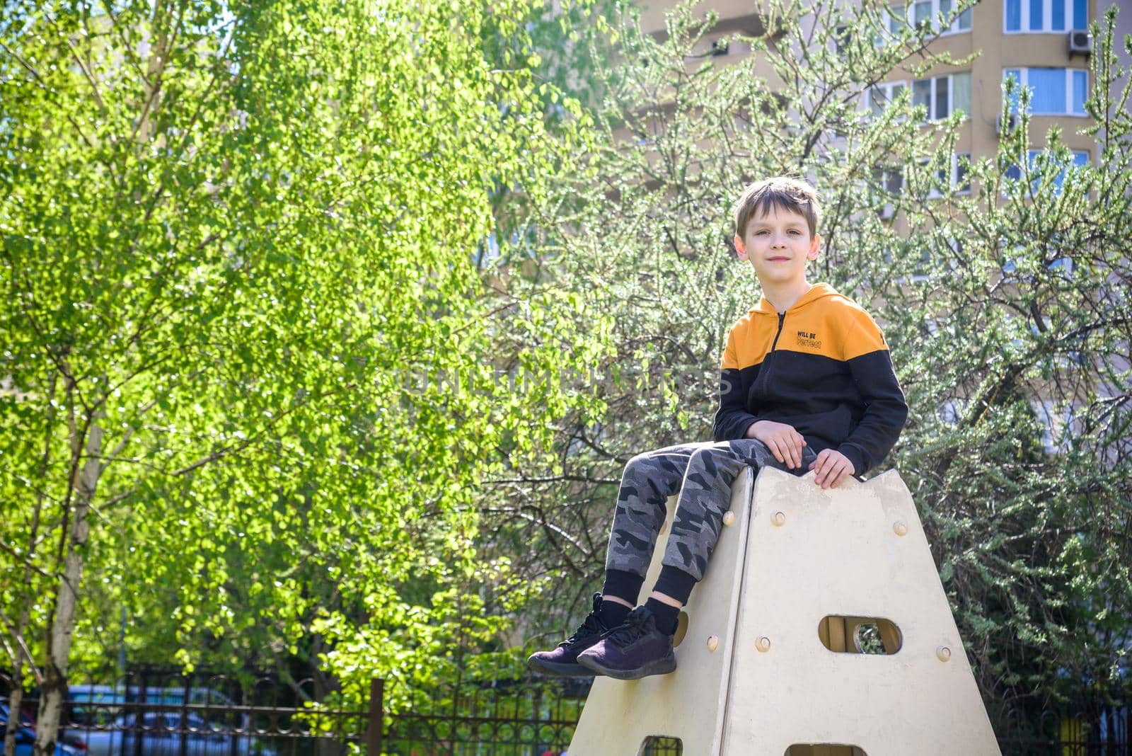 Teenager boy climbing at kid playground outdoor. The climber trains simulator on the street. Healthy leisure for children concept by Kobysh