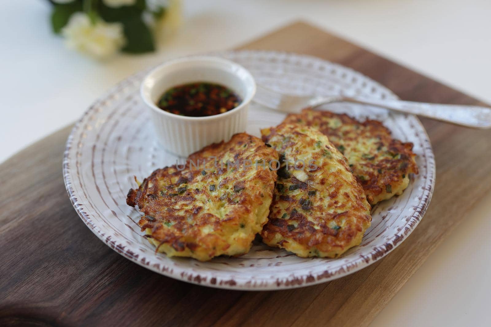 Zucchini fritters, vegetarian zucchini fritters on a white plate served with soy sauce in a small white bowl. Vegetarian food