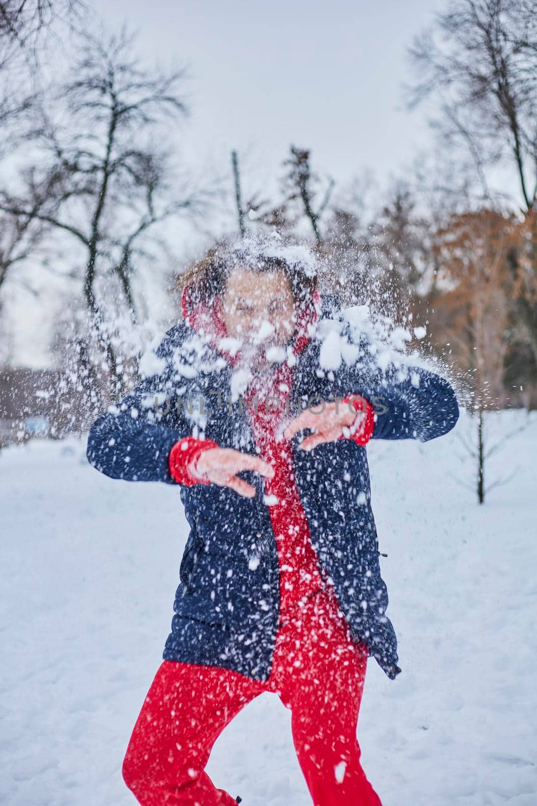 a young happy man is having fun in a winter park, throwing snow, it is cold in his hands, the emissions are off scale