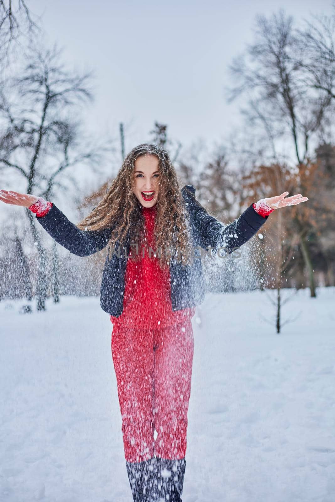 a young happy woman is having fun in a winter park, throwing snow, it is cold in her hands, the emissions are off scale