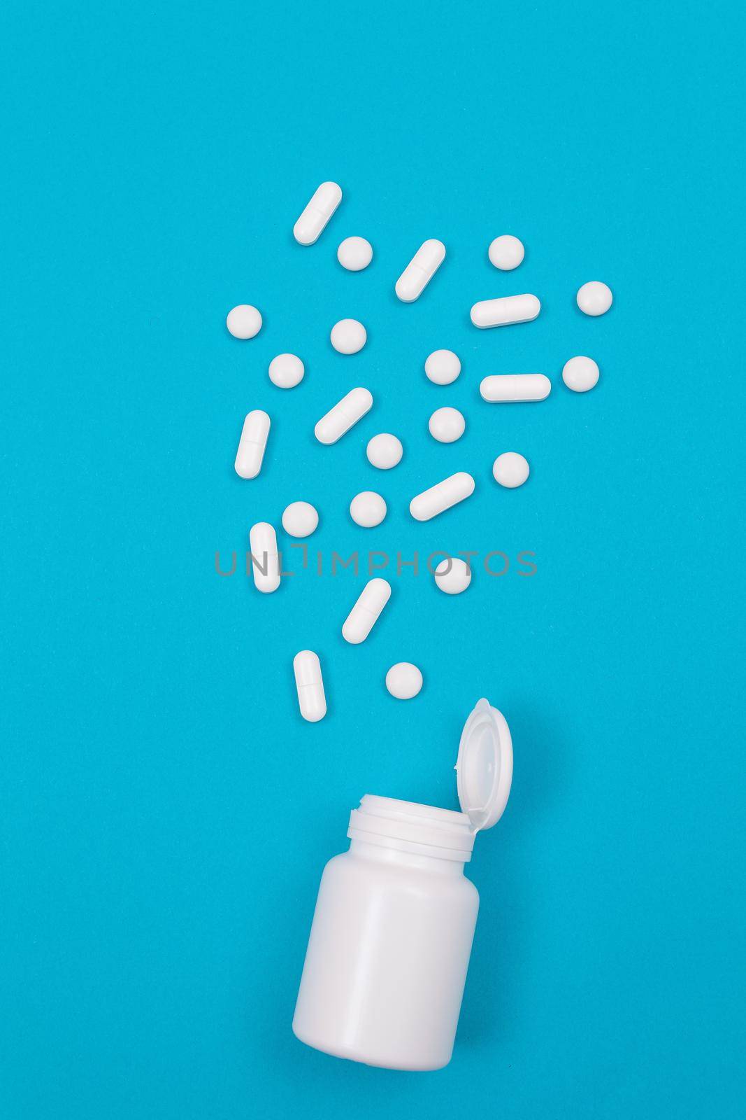 Global Pharmaceutical Industry and Medicinal Products - White Pills or Tablets Scattered from the Pill Container, Lying on Blue Background