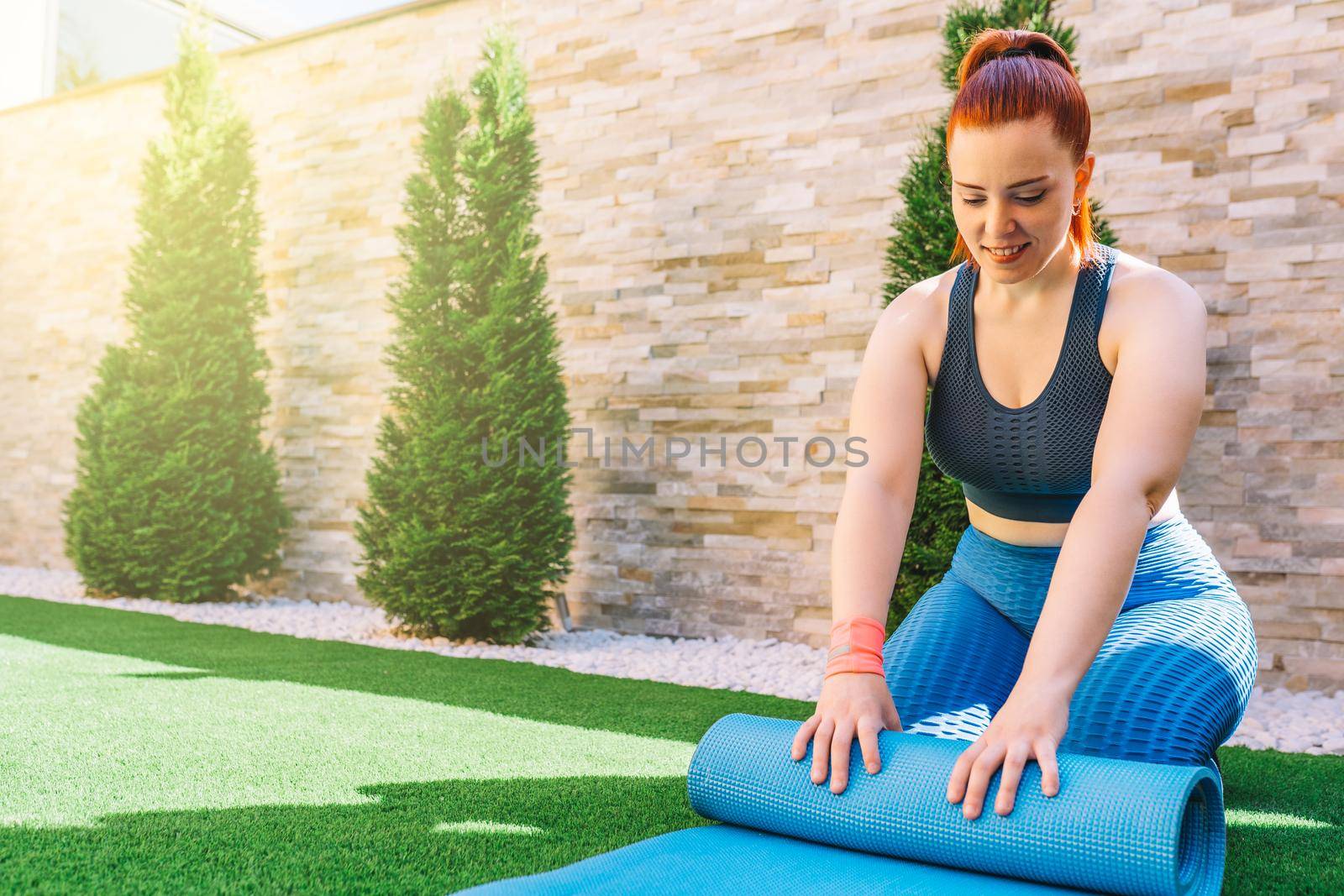 Attractive young fitness girl exercising outdoors in the garden of her home, preparing for stretching exercises. health and wellness concept.natural light in the garden.