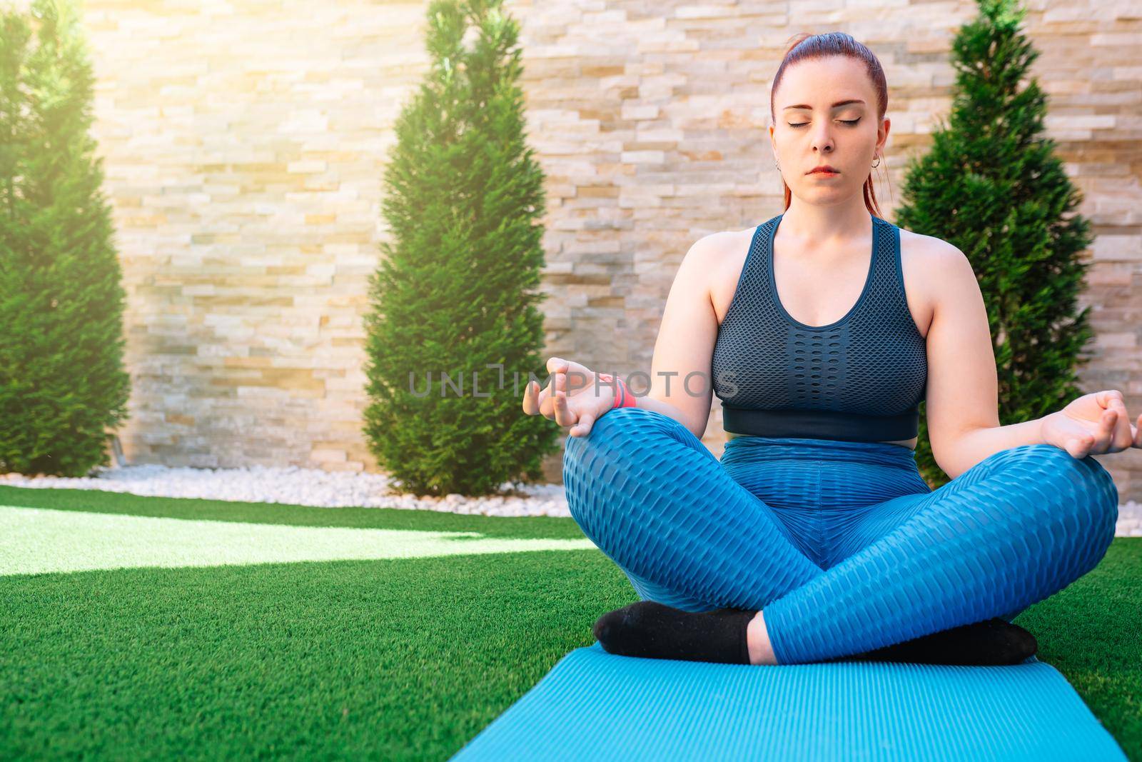 young redheaded fitness woman practising meditation outdoors, in the garden of her house, doing yoga breathing exercises. health and wellness concept. natural light in the garden.