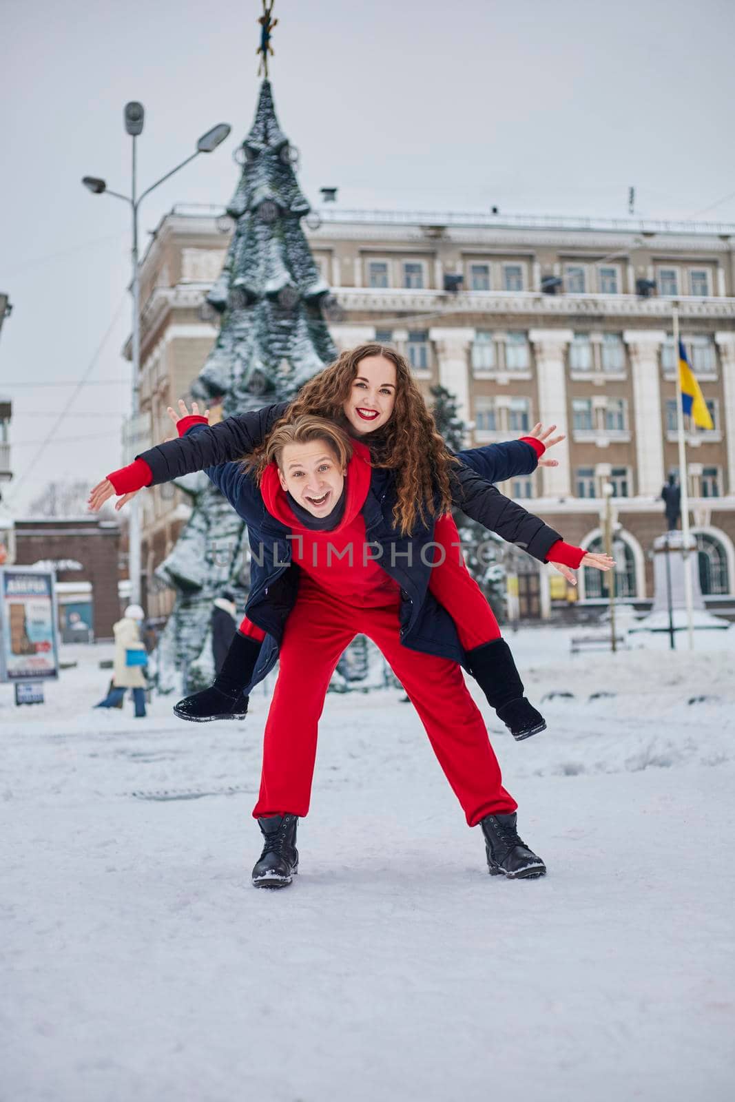 young family guy and girl spend the day in the park on a snowy day. Emotional young couple having fun while walking in the winter city, a lively man hugs his laughing beautiful woman. by mosfet_ua