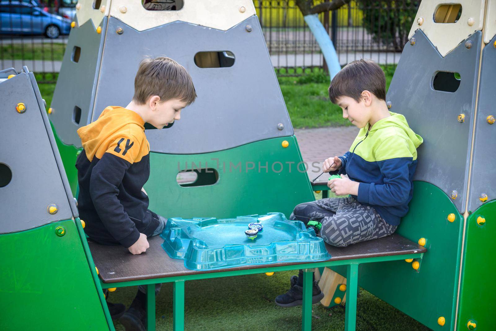 Two Boys playing with modern spin top outdoors. Entertainment game for children. Top, triggered by a trigger. Kids having a tournament on arena or battle field by Kobysh
