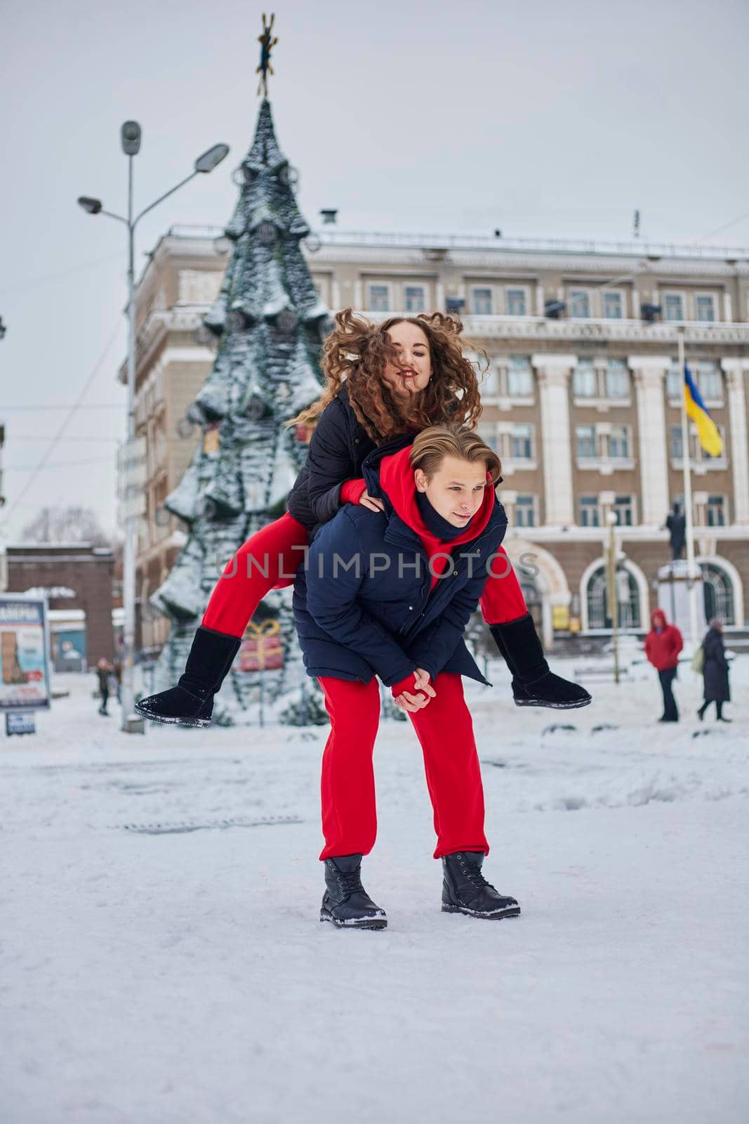 young family guy and girl spend the day in the park on a snowy day. Emotional young couple having fun while walking in the winter city, a lively man hugs his laughing beautiful woman. by mosfet_ua