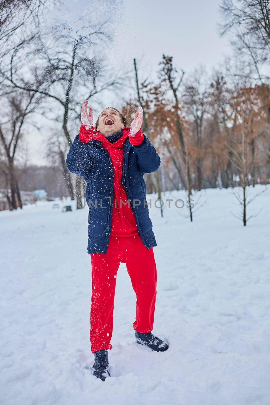 a young happy man is having fun in a winter park, throwing snow, it is cold in his hands, the emissions are off scale. by mosfet_ua