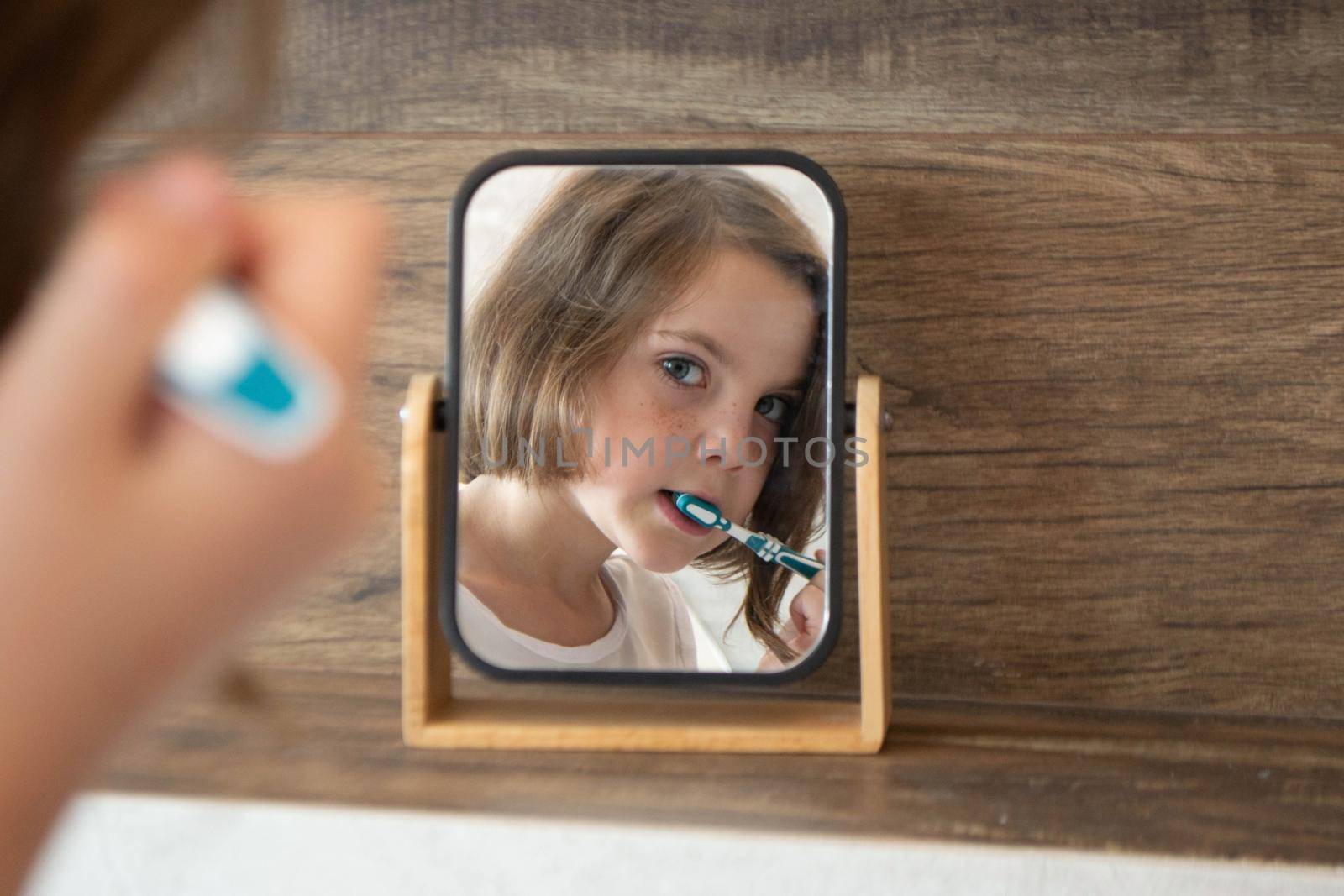 Oral hygiene, healthy teeth and care. Girl brushing teeth with toothbrush and looking in mirror in bathroom interior in the morning, closeup, empty space. High quality photo