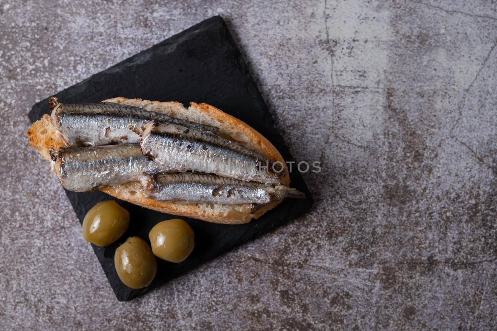 tapa of sardines on a slice of bread with tomato and olives on black slate typical Spanish