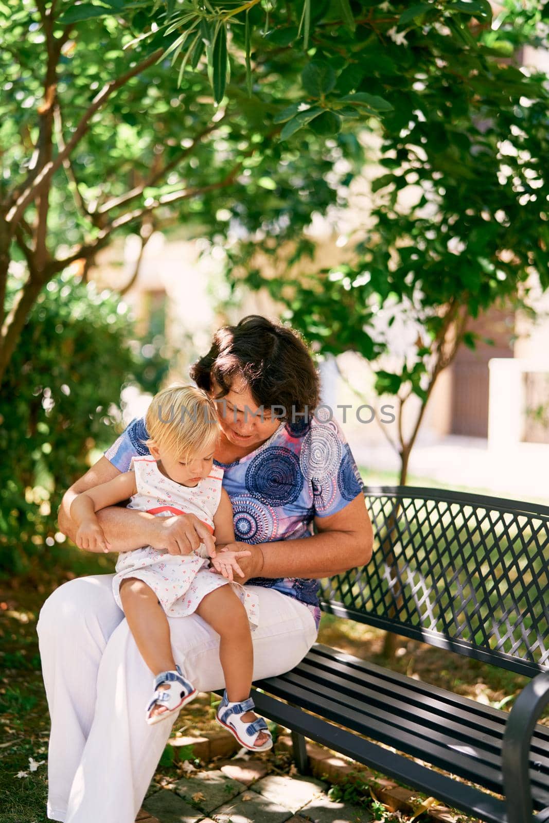 Grandmother sits on a bench with her little granddaughter in her arms. High quality photo