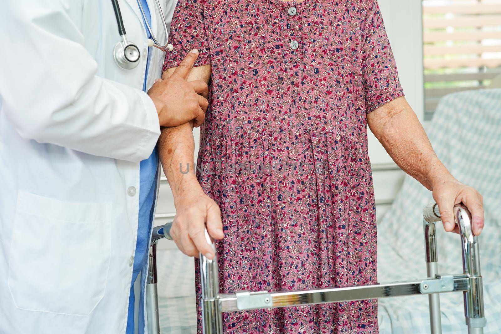 Doctor help Asian elderly woman disability patient walk with walker in nursing hospital, medical concept.