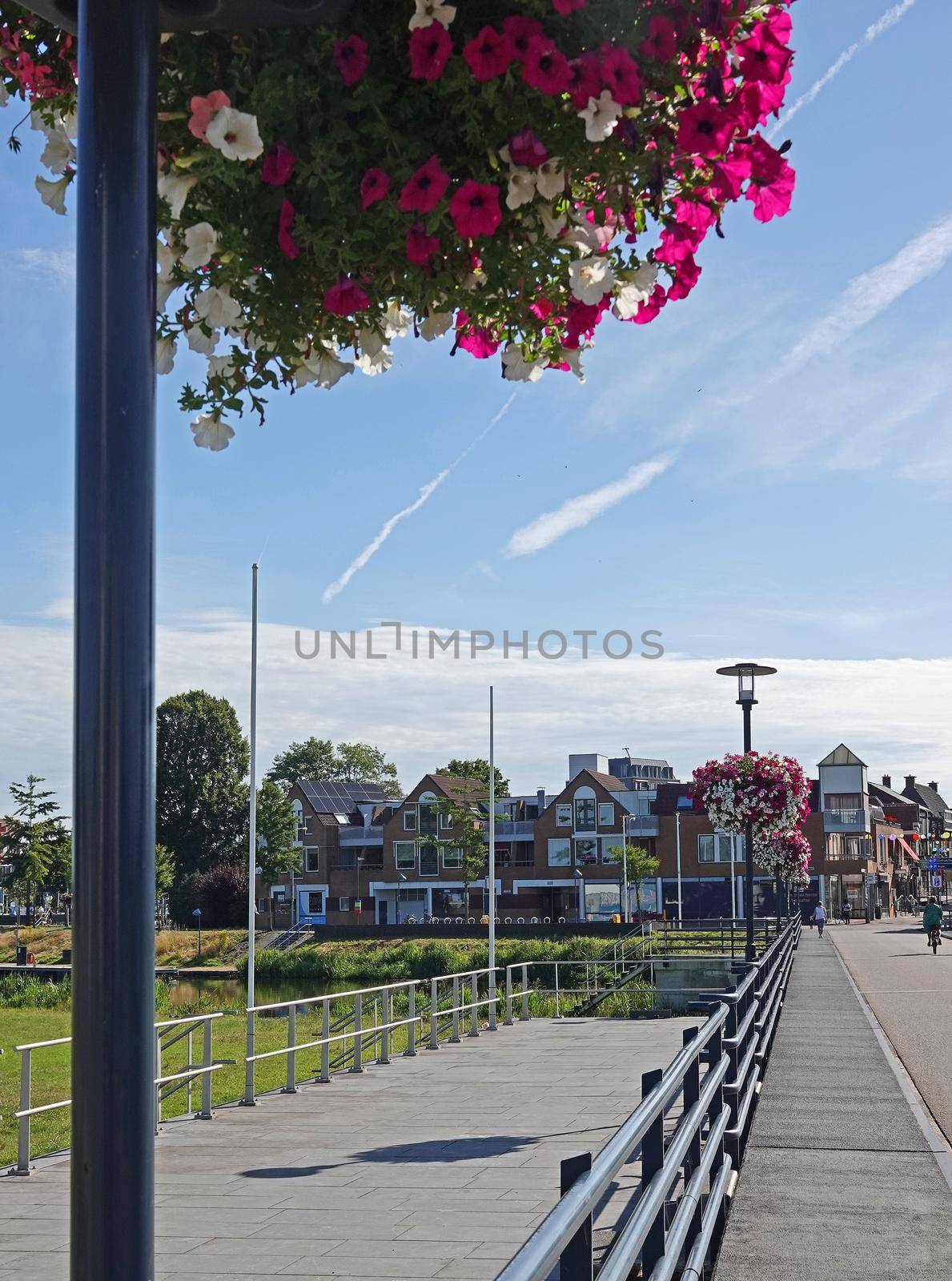 July 17 2022 Hardenberg - Netherlands Flower baskets on the lampposts on a bridge in the Dutch town Hardenberg. The baskets contain pink and white petunias and pink geraniums. In the distance a row of houses and some people.