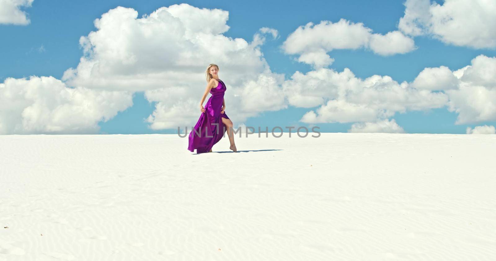 Cinematic slow motion of a woman walking on a sand dune. Barefoot woman traveler in a dress swinging in the wind on the undulating surface of the sandy desert with a cloud in the background. 4K Scenic nature.
