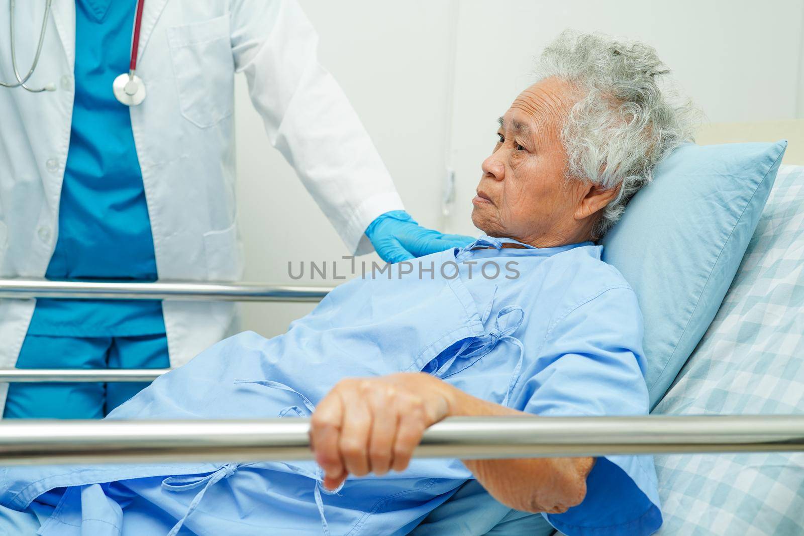 Asian elder senior woman patient holding bed rail while lie down with hope waiting her family in hospital.