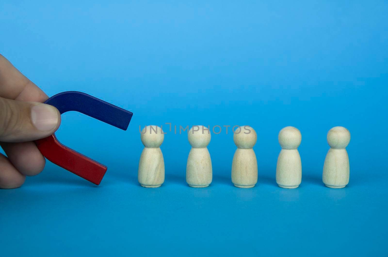 Hand holding magnet attracting wooden doll figures on blue background. Business and law of attraction concept