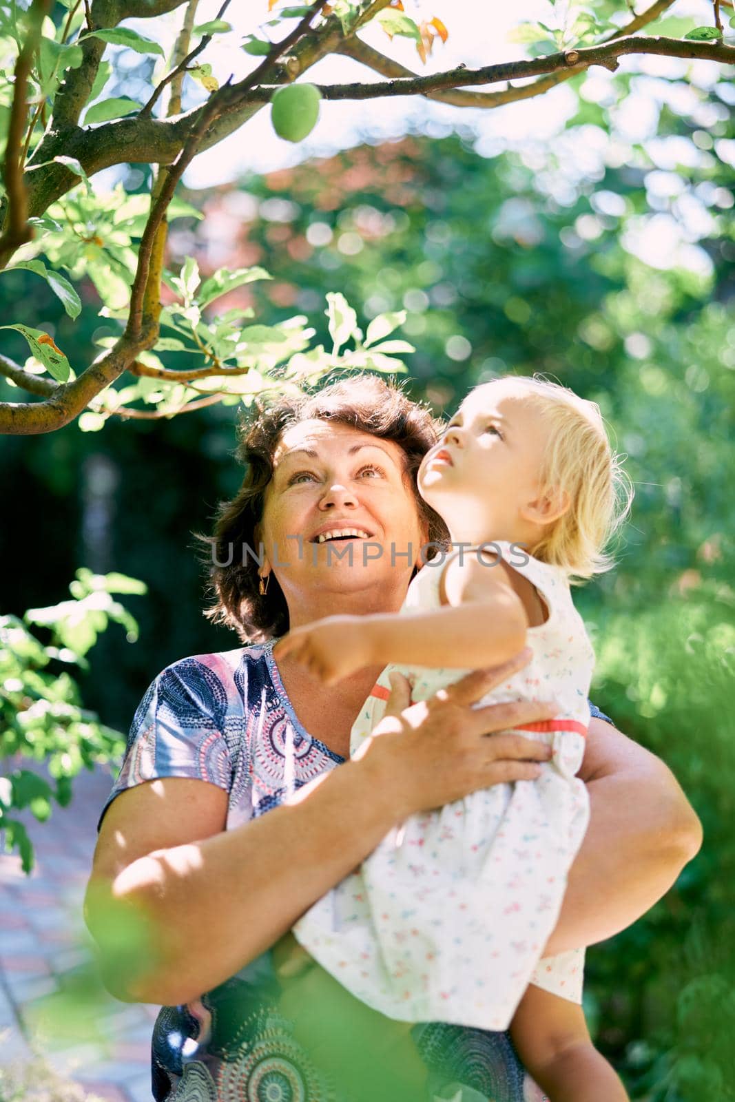 Woman holding a little girl in her arms and looking up by Nadtochiy