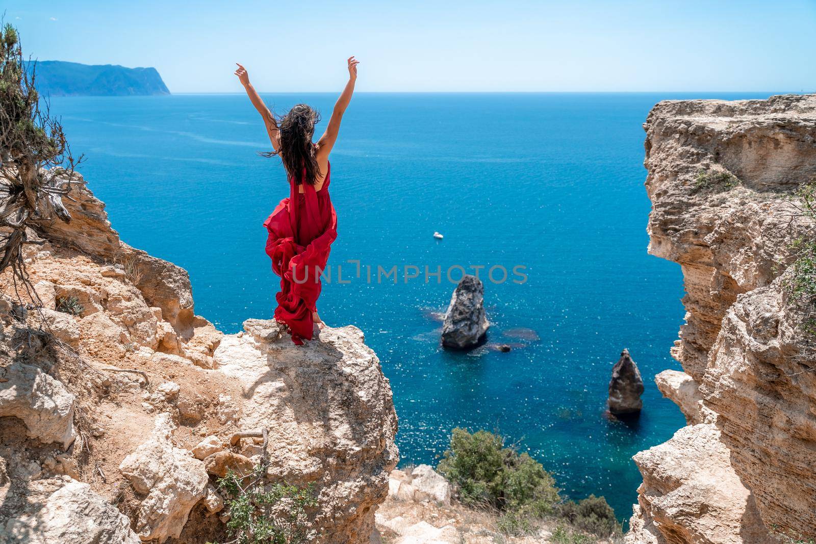 A woman in a red flying dress fluttering in the wind, against the backdrop of the sea. by Matiunina