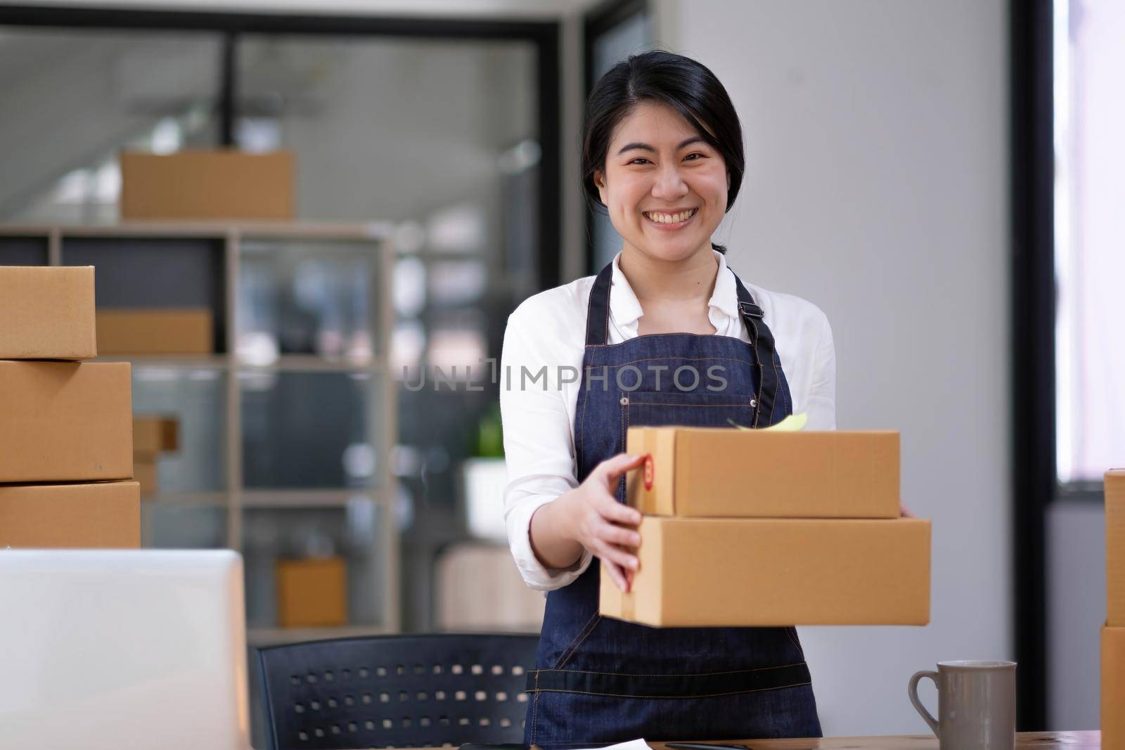 Startup small business entrepreneur of freelance Asian woman using a laptop with box Cheerful success Asian woman her hand lifts up online marketing packaging box and delivery SME idea concept by wichayada