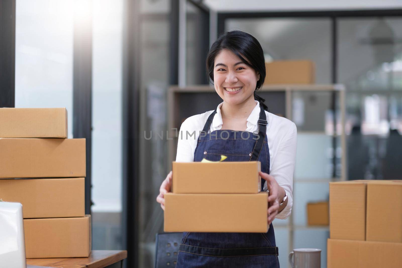 Startup small business entrepreneur of freelance Asian woman using a laptop with box Cheerful success Asian woman her hand lifts up online marketing packaging box and delivery SME idea concept by wichayada