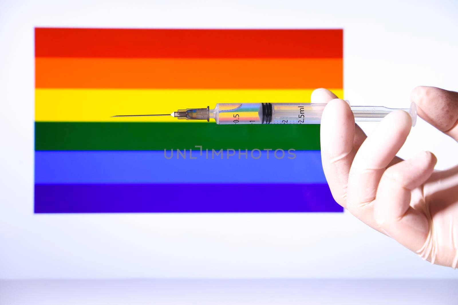 Hand holding syringe and rainbow flag in the background by soniabonet