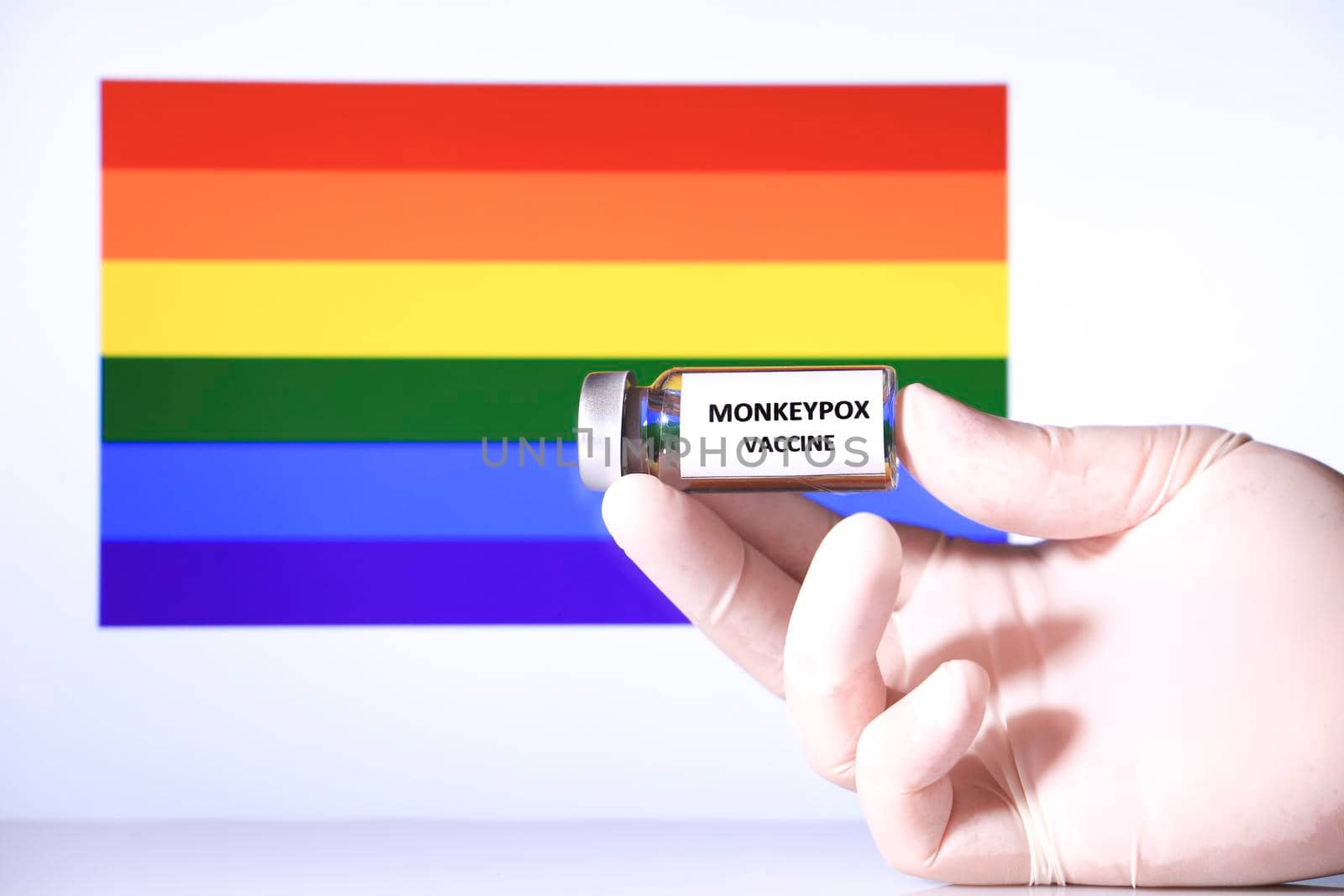 Hand holding vial with monkeypox vaccine. Rainbow flag in the background.