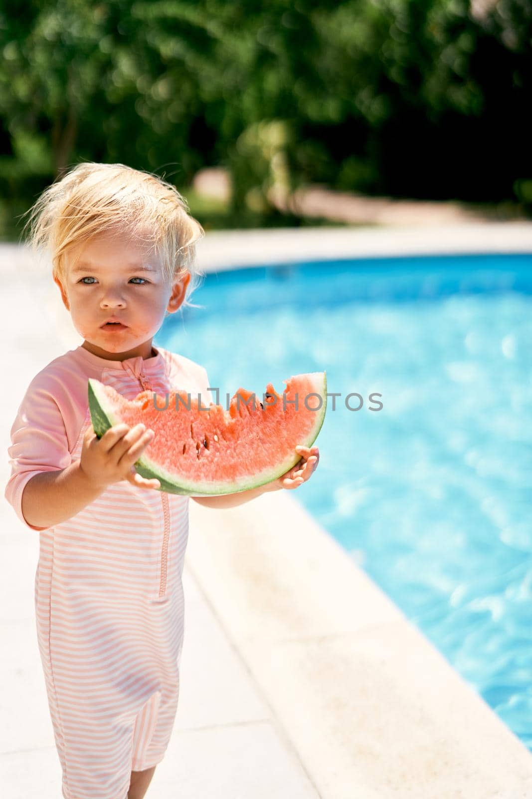 Little girl with a piece of a watermelon near the pool with turquoise water by Nadtochiy