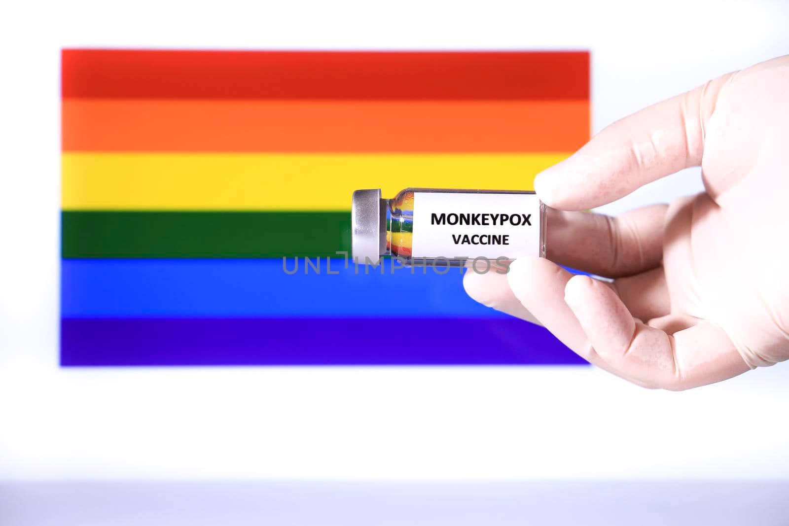 Hand holding vial with monkeypox vaccine. Rainbow flag in the background.