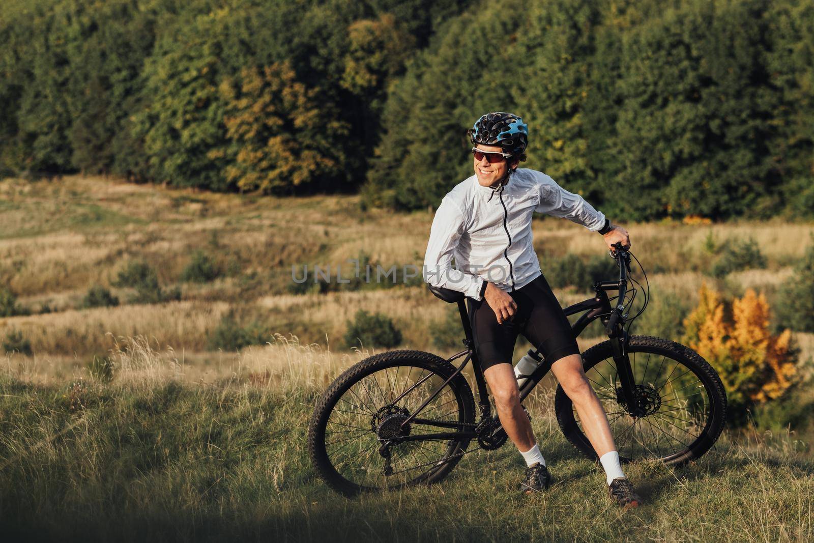 Professional Male Cyclist Leans on Bike and Adult Man Enjoying Rest During His Ride on Bicycle