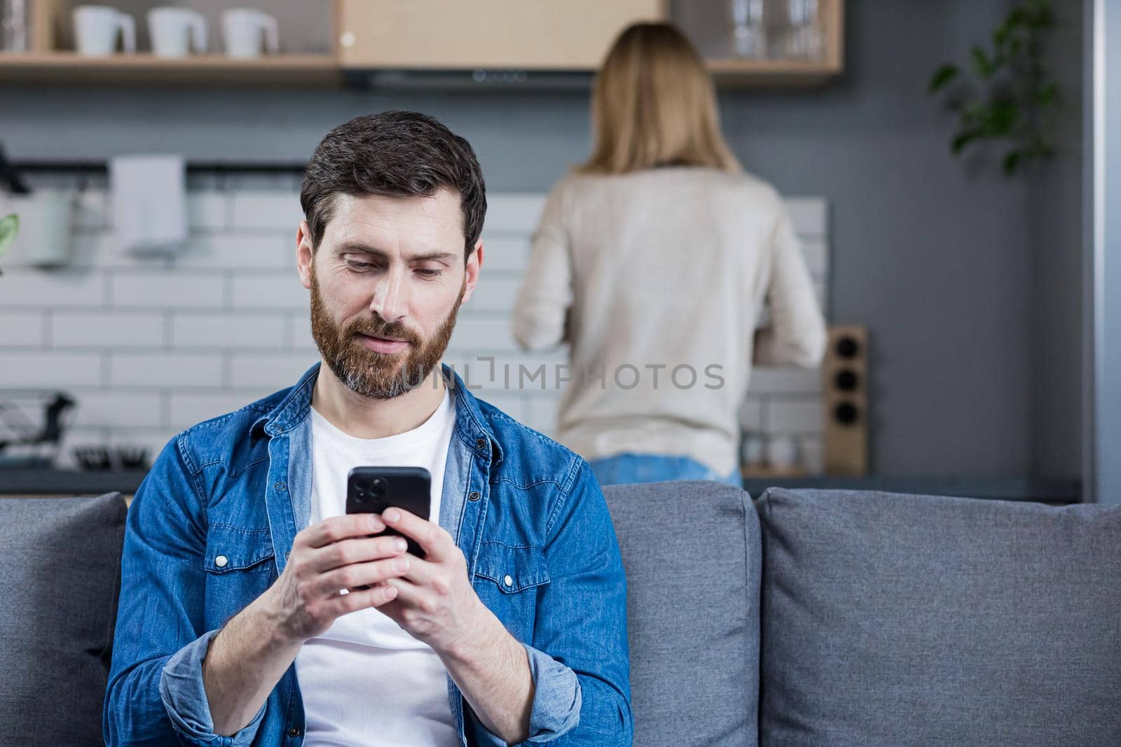 Close up photo. Conflict, young couple, family, man and woman. The man sits on the couch, looks at the phone, plays games, does not pay attention to the woman, avoids