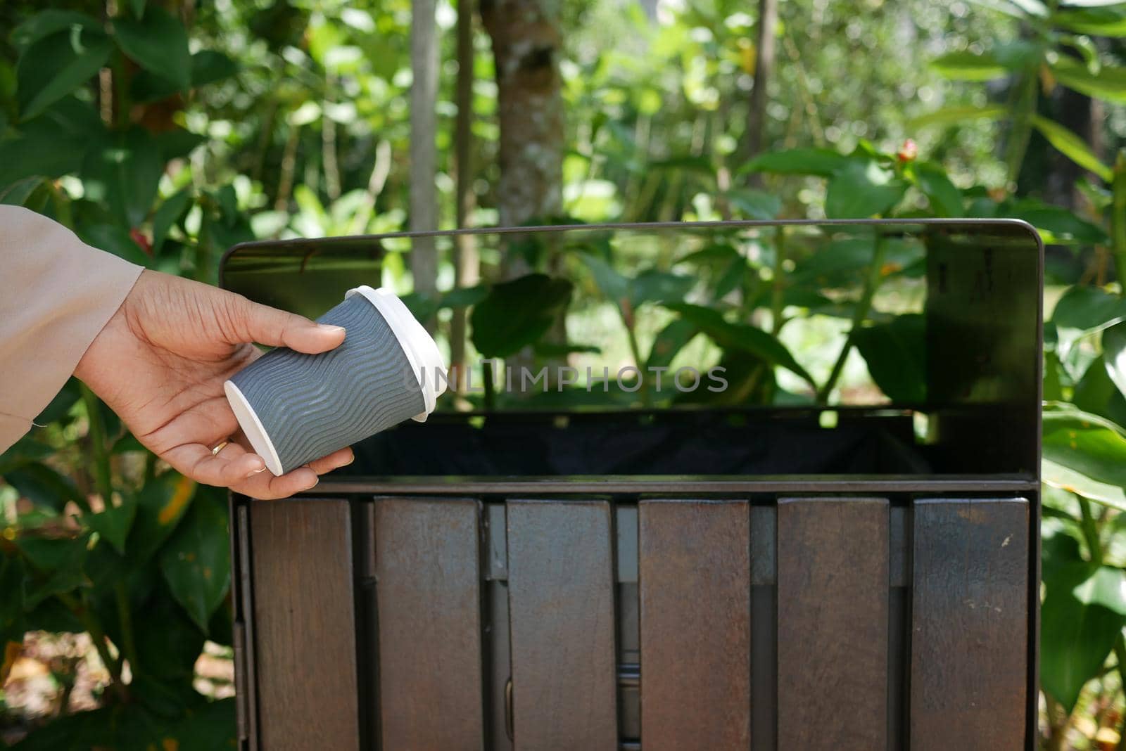 women hand throwing an empty paper coffee cup in the garbage trash or bin,