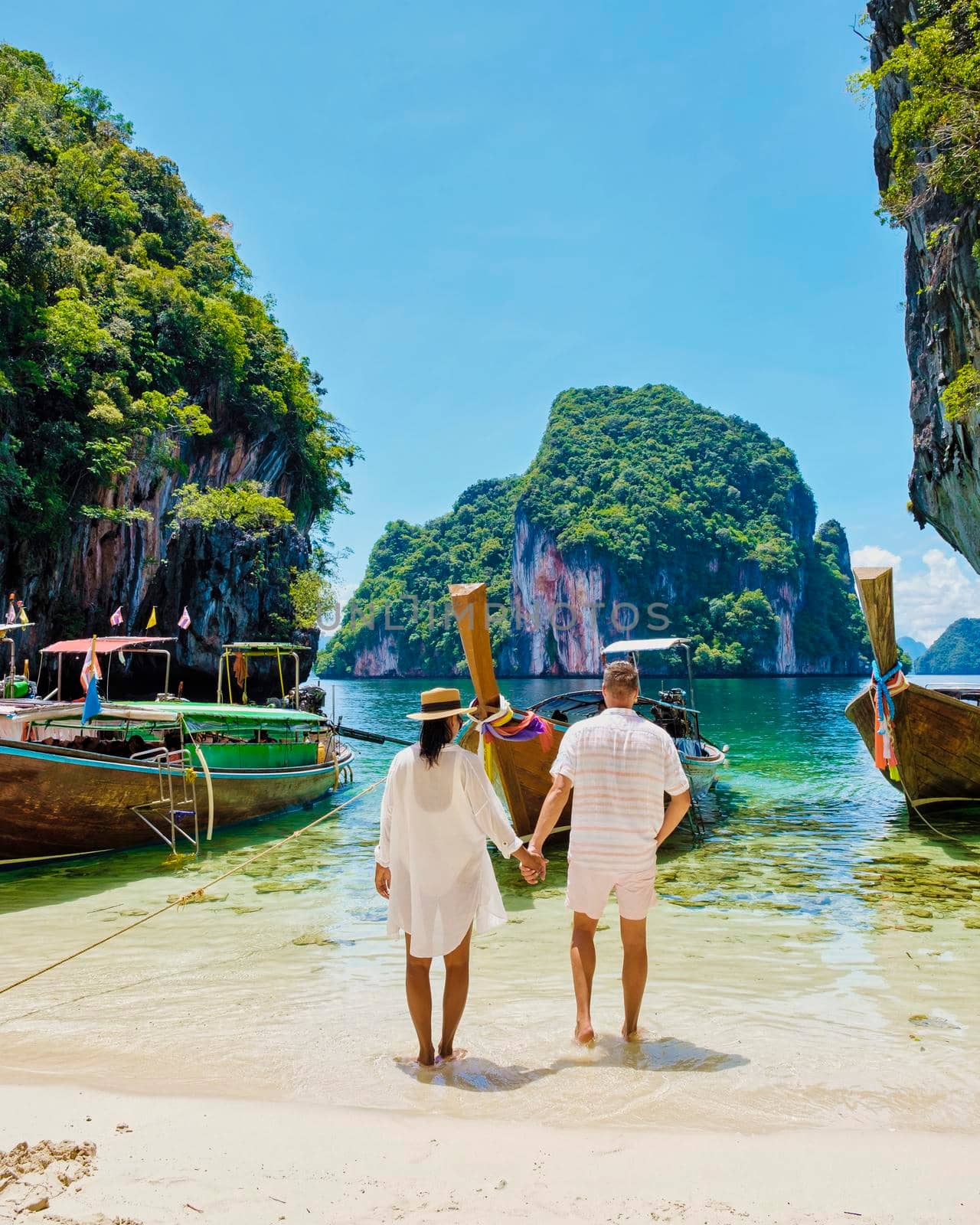 Koh Lao Lading near Koh Hong Krabi Thailand, beautiful beach with longtail boats, a couple of European men, and an Asian woman on the beach.