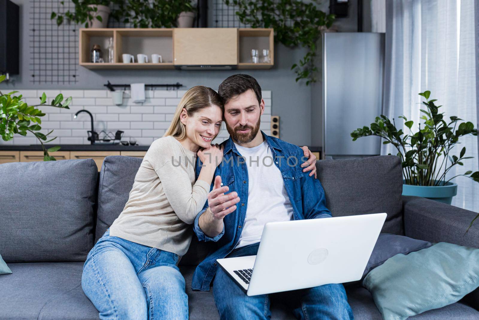 Married couple man and woman sitting together at home on the couch using laptop for video chat and chatting with friends
