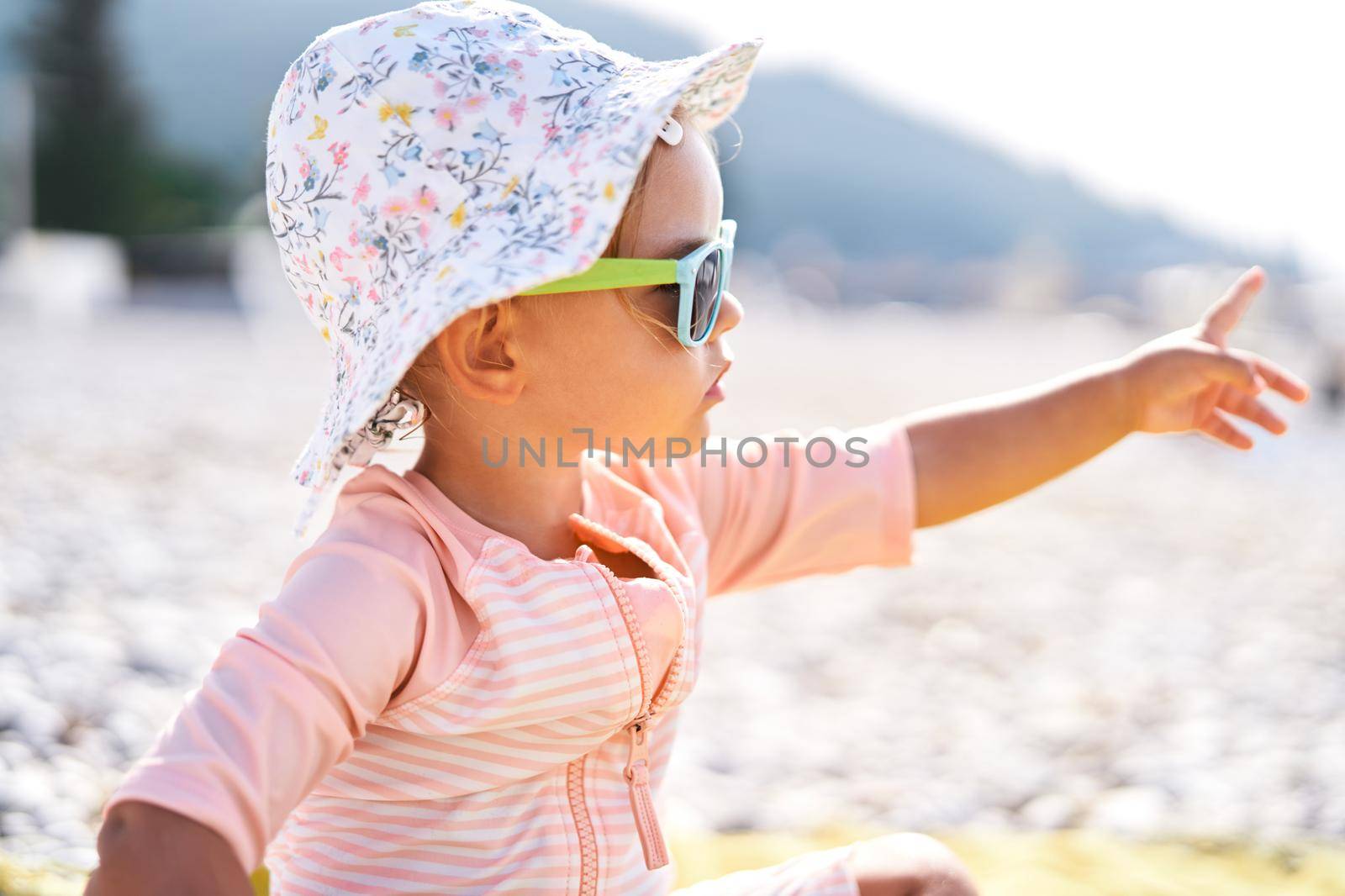 Little girl in sunglasses on the beach pointing her finger into the distance. High quality photo