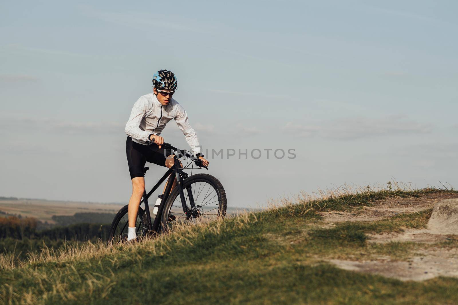 Equipped Professional Male Cyclist Riding Mountain Bike on Top of Hill, Copy Space on Sky Background