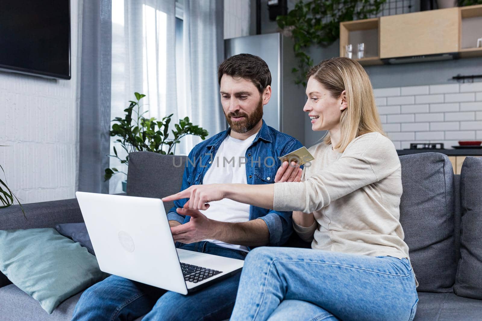 Online shopping. Man and woman shopping online from a notebook, holding a credit card in his hands. A purchase for a woman she chose herself. At home, sitting on the couch. Happy, satisfied