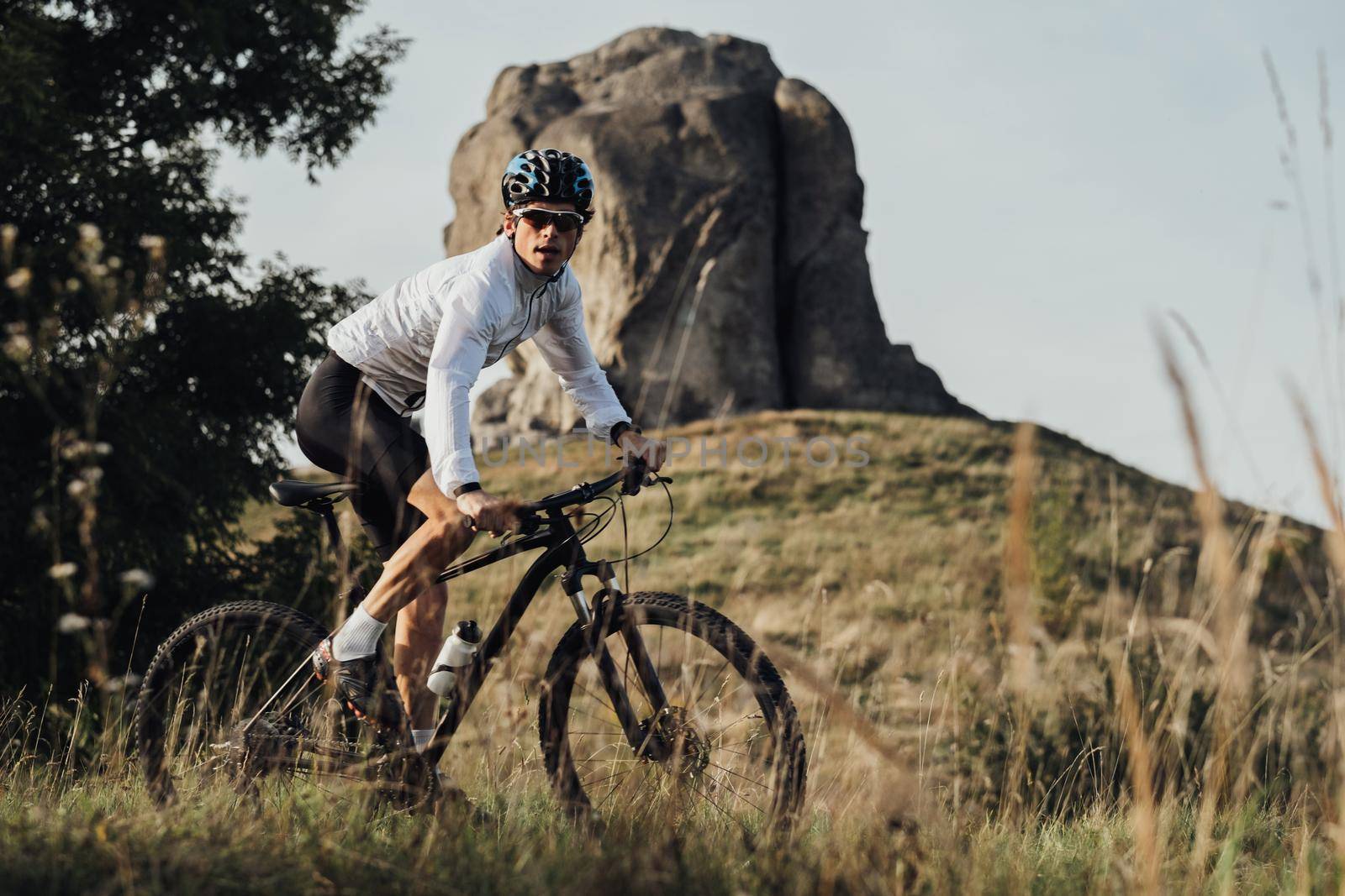 Professional Equipped Cyclist on Trail with Giant Stone, Miracle of Nature on Background, Adult Man Riding Bike Outdoors