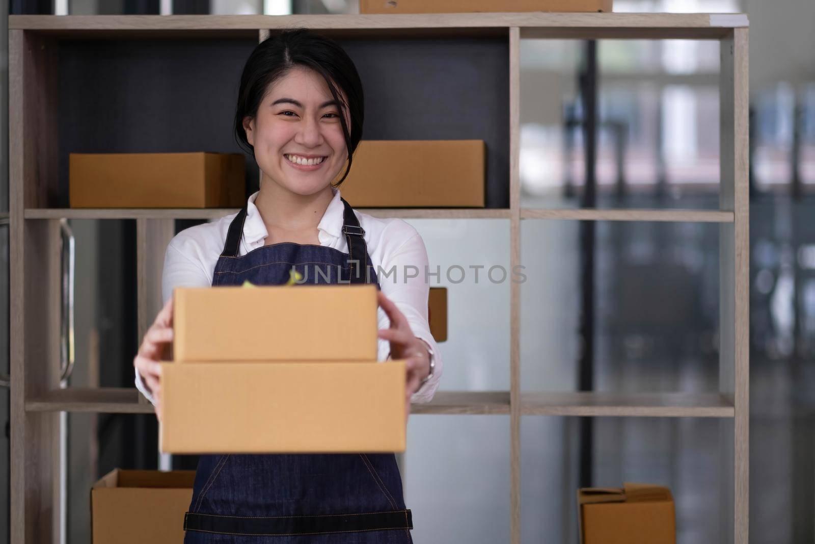 Startup small business entrepreneur of freelance Asian woman using a laptop with box Cheerful success Asian woman her hand lifts up online marketing packaging box and delivery SME idea concept by wichayada