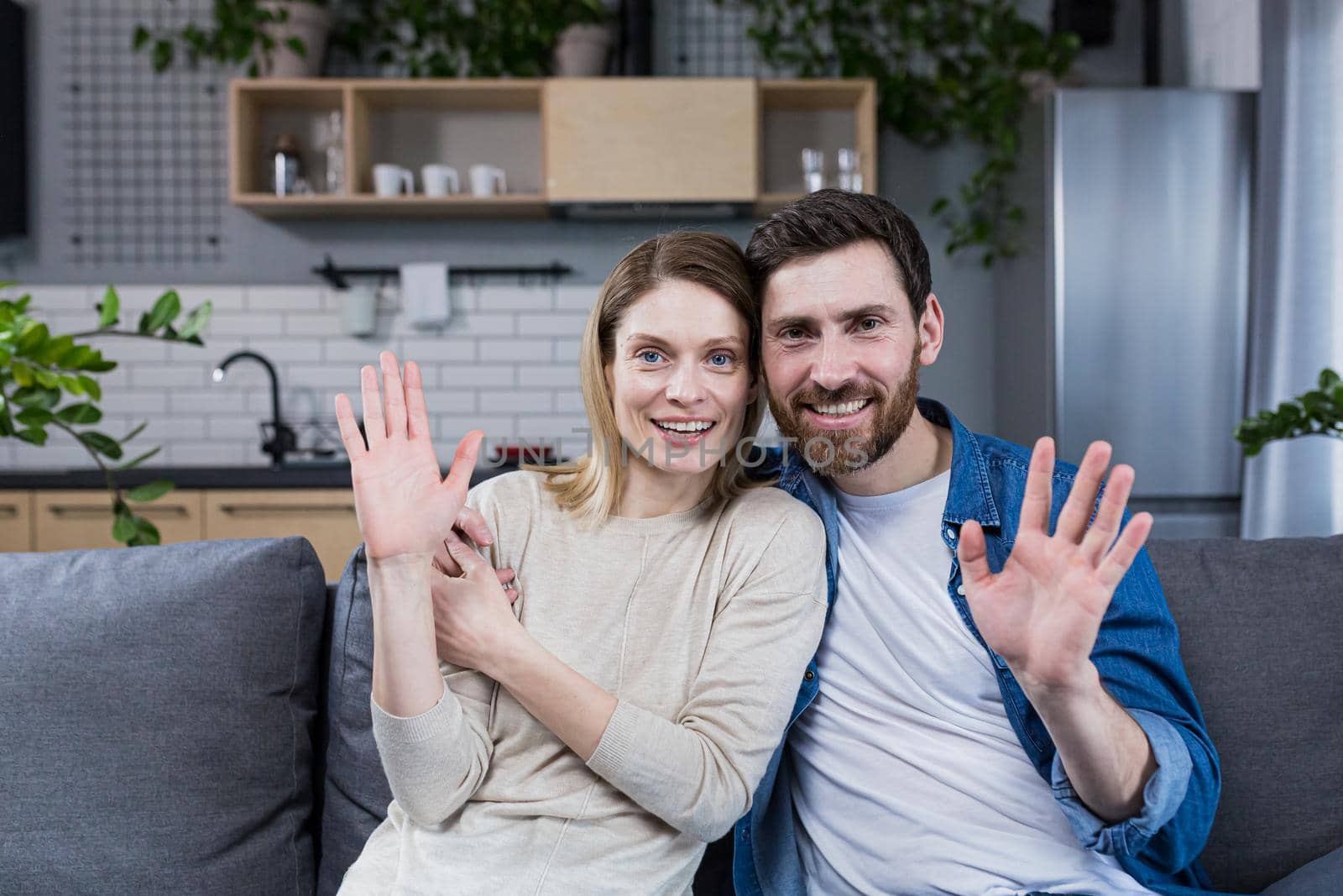 Portrait of a happy young family, couple. Man and woman sitting on sofa, hugging, waving, smiling, looking at camera, looking at each other