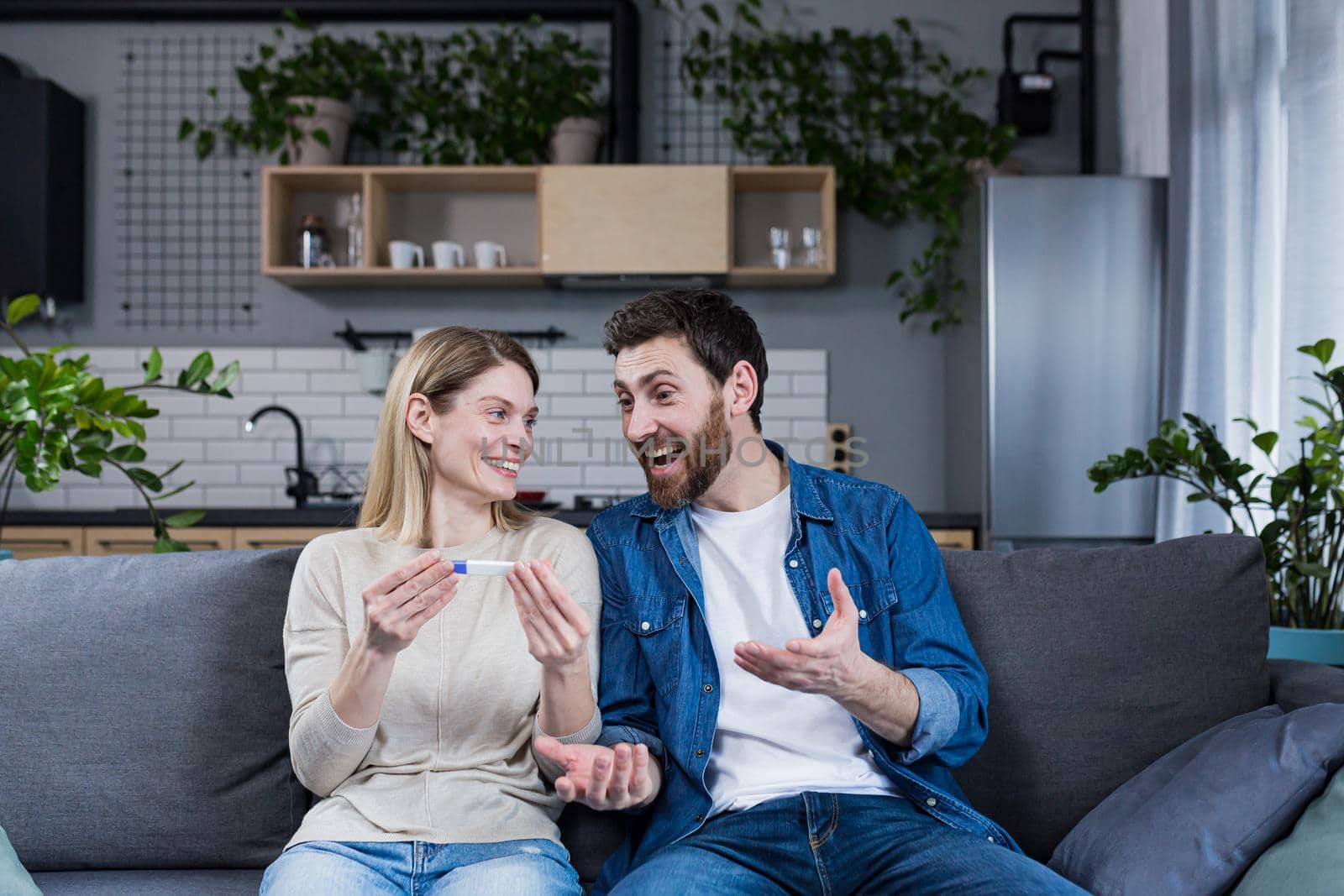 Happy couple man and woman on the couch sitting and rejoicing in a positive pregnancy test