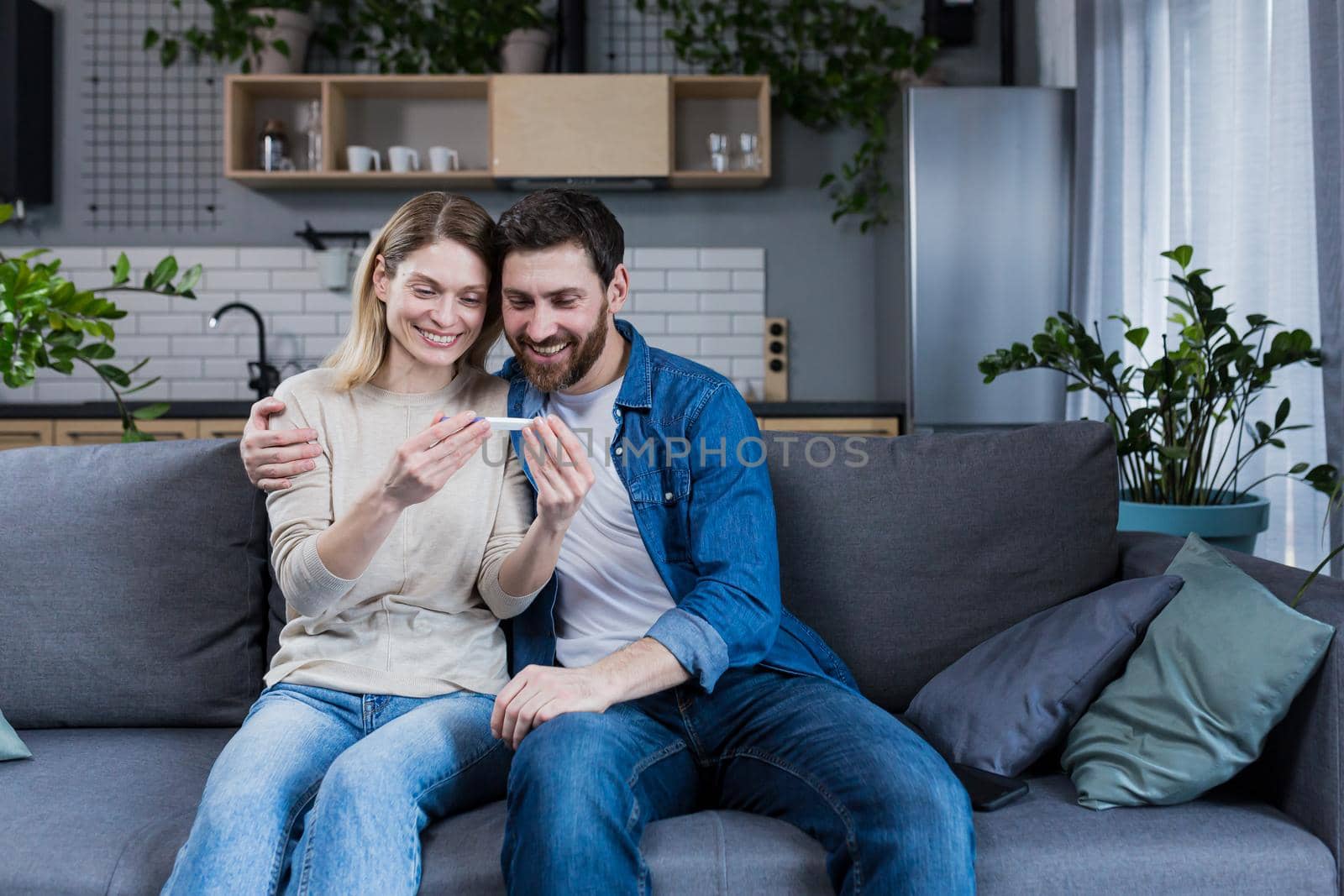 Happy couple man and woman on the couch sitting and rejoicing in a positive pregnancy test