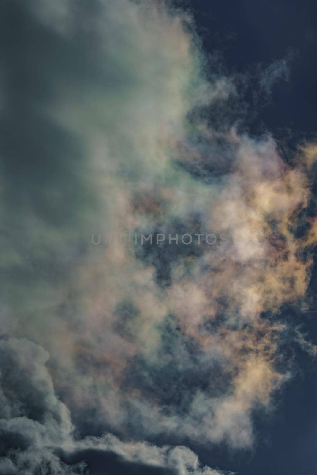 Diffraction of light on drops of supercooled water in clouds, rainbow clouds against the blue sky in clear sunny weather, irisation of cumulus clouds, optical phenomenon, spectral colors. High quality photo